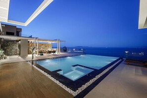 A modern infinity pool with a clear view of the ocean, a covered seating area, and a stone wall.