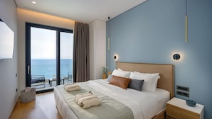 Ein modernes Hotelzimmer mit einem großen Bett, einem Nachttisch und Meerblick durch eine Schiebetür.