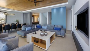 Ein modernes Wohnzimmer mit einem großen Fernseher, grauen Sofas und einem weißen Couchtisch.