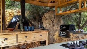 A rustic outdoor kitchen with a stone wall, wooden cabinetry, and a built-in grill. - Unique 4 bedroom villa with total privacy (Agios Nikolaos)