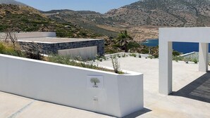 A modern building with a white facade, a sign labeled "LYRA," and a view of a mountainous landscape and sea.