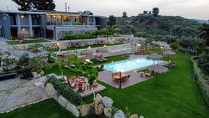 A modern outdoor pool area with seating and a well-maintained lawn, surrounded by a stone wall and lush greenery. - Exclusive 9 bedrooms | heated pool (Perivolia)