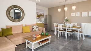 A modern living room with a beige sofa, a wooden coffee table, and a dining area with white chairs and a wooden table. - Exclusive 9 bedrooms | heated pool (Perivolia)