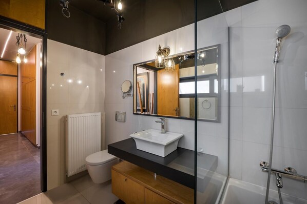Une salle de bain moderne avec une douche à l’italienne en verre, un lavabo blanc et un meuble-lavabo en bois.