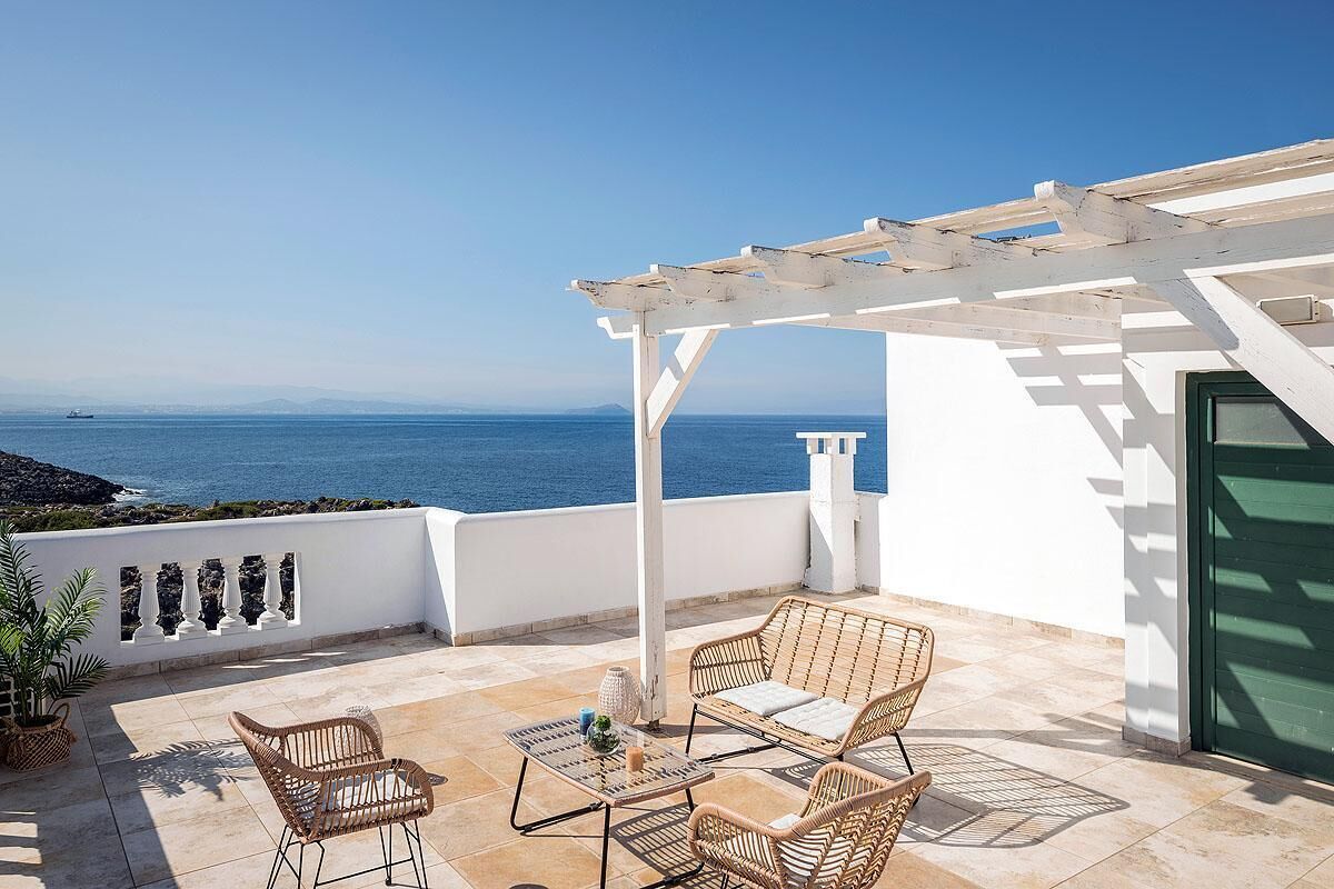 Een terras met rieten meubilair, een pergola en uitzicht op zee.