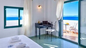 Ein Hotelzimmer mit einem Bett, einem Schreibtisch mit einem Laptop, einem Stuhl und Meerblick durch ein großes Fenster.