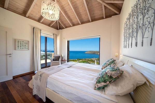 A bedroom with a large bed, a view of the sea, and a wooden ceiling.