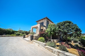 A modern house with a stone facade, a covered porch, and a well-maintained garden with various plants and flowers.