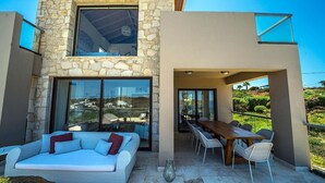 Ein modernes Haus mit Naturstein-Fassade, einer Glastür, die zu einem Essbereich im Freien führt, und einer Couch mit Kissen.