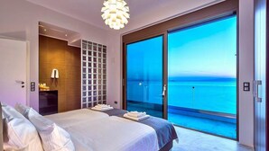 Quarto moderno com uma cama grande, estante embutida e porta de vidro deslizante que dá para uma varanda com vista para o mar.