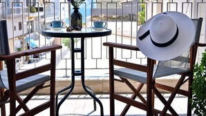 Ein Balkon mit zwei Holzstühlen, einem kleinen runden Tisch, einer Blumenvase und einem weißen Hut auf einem der Stühle.