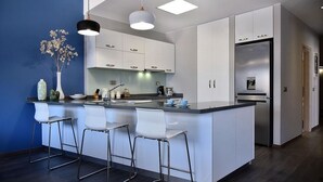Eine moderne Küche mit weißen Schränken, einer zentralen Kochinsel mit Barhocker, einem eingebauten Backofen und einem Kühlschrank.
