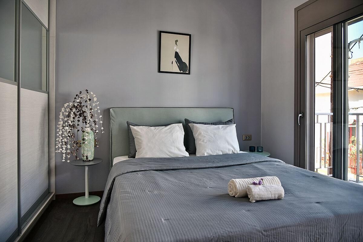 Quarto moderno com uma cama grande, uma pequena mesa de cabeceira com um vaso e um quadro na parede.