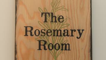 A square wooden sign with the text "The Rosemary Room" and a green rosemary plant illustration.