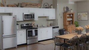 Een moderne keuken met witte kasten, roestvrijstalen apparatuur en een houten eettafel met stoelen.