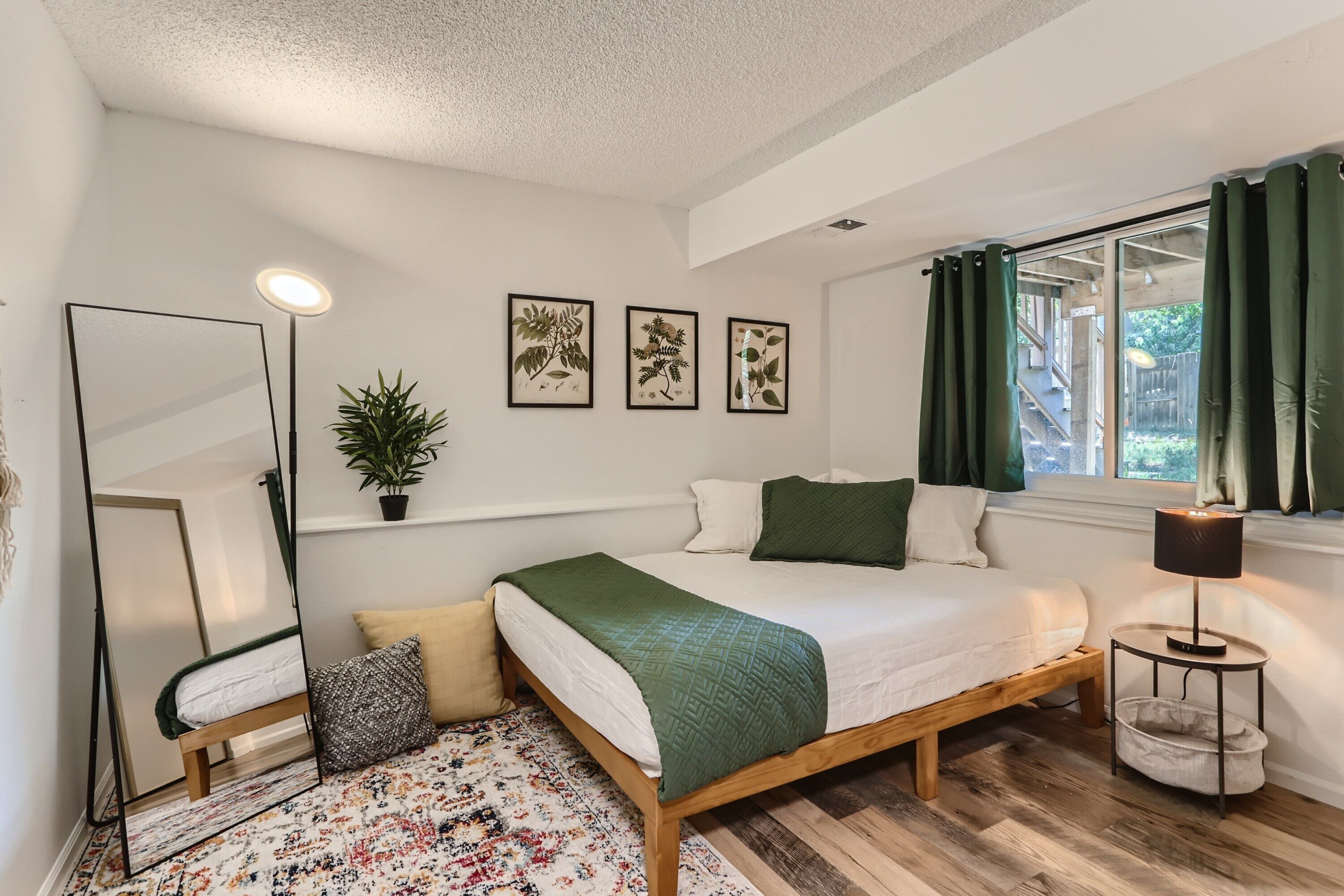 A bedroom with a bed, a mirror, a potted plant, and framed botanical prints on the wall.