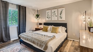 A bedroom with a bed, a nightstand, a lamp, a hanging plant, and three framed botanical prints on the wall. - Charming Bungalow - Longmont- Nearby Lyons Pet Friendly fenced yard (Longmont)