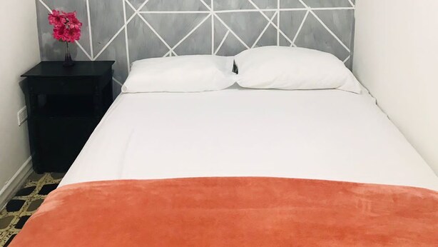 Una cama con un cabecero de estampado geométrico, una almohada blanca y un plaid naranja.