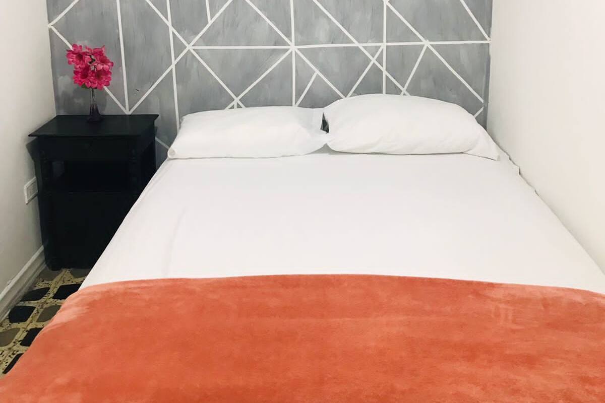A bed with a geometric-patterned headboard, a white pillow, and an orange throw blanket.