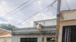 Un edificio de dos pisos con fachada de hormigón, una ventana con rejas y una puerta metálica.