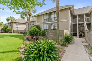 A multi-story residential building with a well-maintained lawn, various shrubs, and a gated entrance.