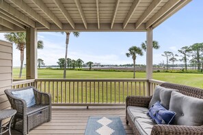 A covered porch with wicker furniture and a view of a golf course.