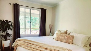 Un dormitorio con una cama grande, una planta en maceta y vistas a un área exterior por una puerta corrediza.