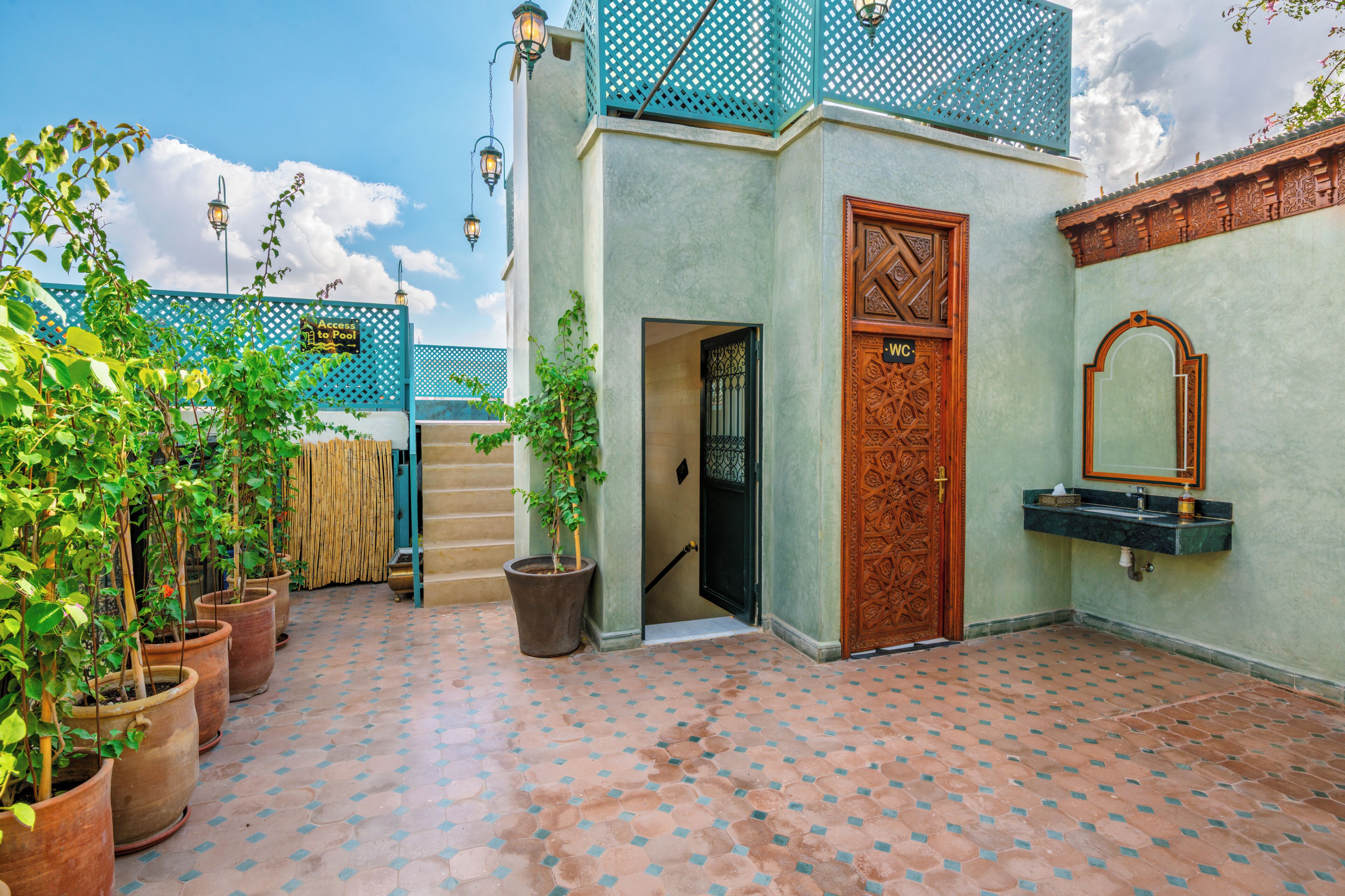 A courtyard with potted plants, a wooden door, a sink, and a staircase leading to an upper level.