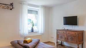 A bedroom with a bed, a dresser, a television, and a window with curtains. - 2 bedroom amazing apartment in Loxstedt (Loxstedt)