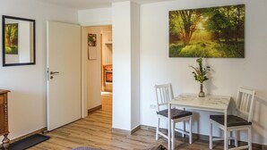 A dining area with a white table and chairs, a vase with flowers, and a painting of a forest scene on the wall. - 2 bedroom amazing apartment in Loxstedt (Loxstedt)