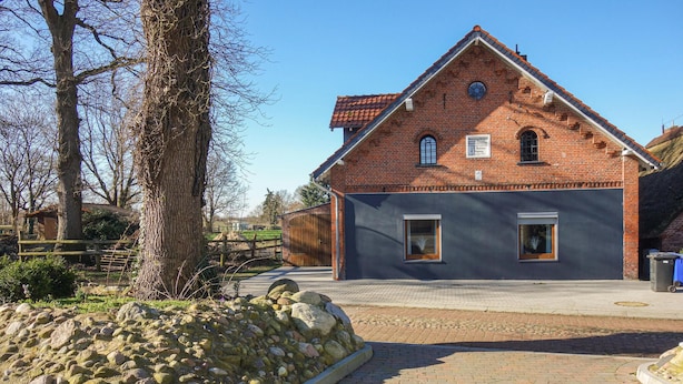 A traditional brick building with a gabled roof, a stone wall in the foreground, and a paved area leading to the entrance. - 2 bedroom amazing apartment in Loxstedt (Loxstedt)
