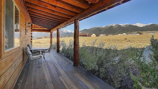Una terraza de madera con una mesa y sillas, con vista a un paisaje montañoso.