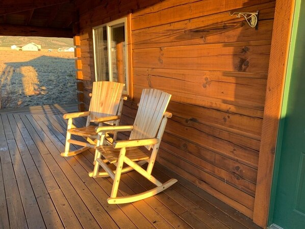 A wooden rocking chair on a porch with a wooden cabin in the background.