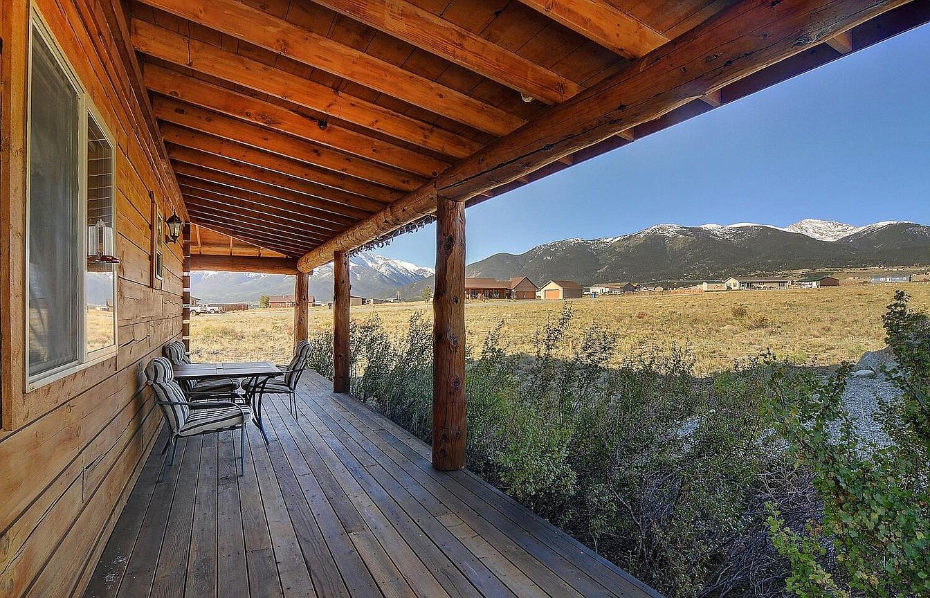 Une terrasse en bois avec une table et des chaises, offrant une vue sur un paysage montagneux.