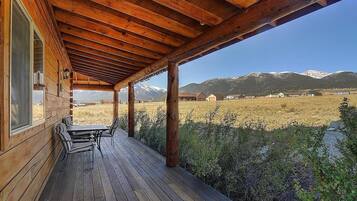 Une terrasse en bois avec une table et des chaises, offrant une vue sur un paysage montagneux.