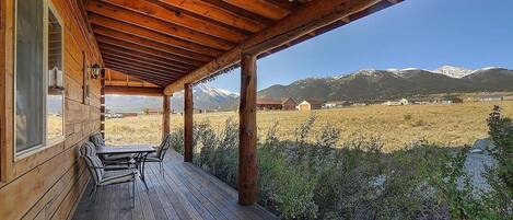 Eine Holzterrasse mit Tisch und Stühlen, mit Blick auf eine gebirgige Landschaft.