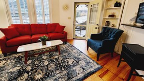 Un salon avec un canapé rouge, un fauteuil bleu, une table basse et un tapis à motifs.