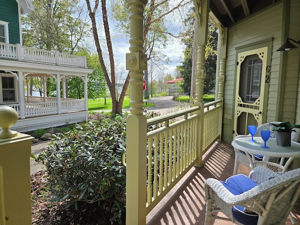 A porch with a white railing, a small table with blue cushions, and a potted plant.