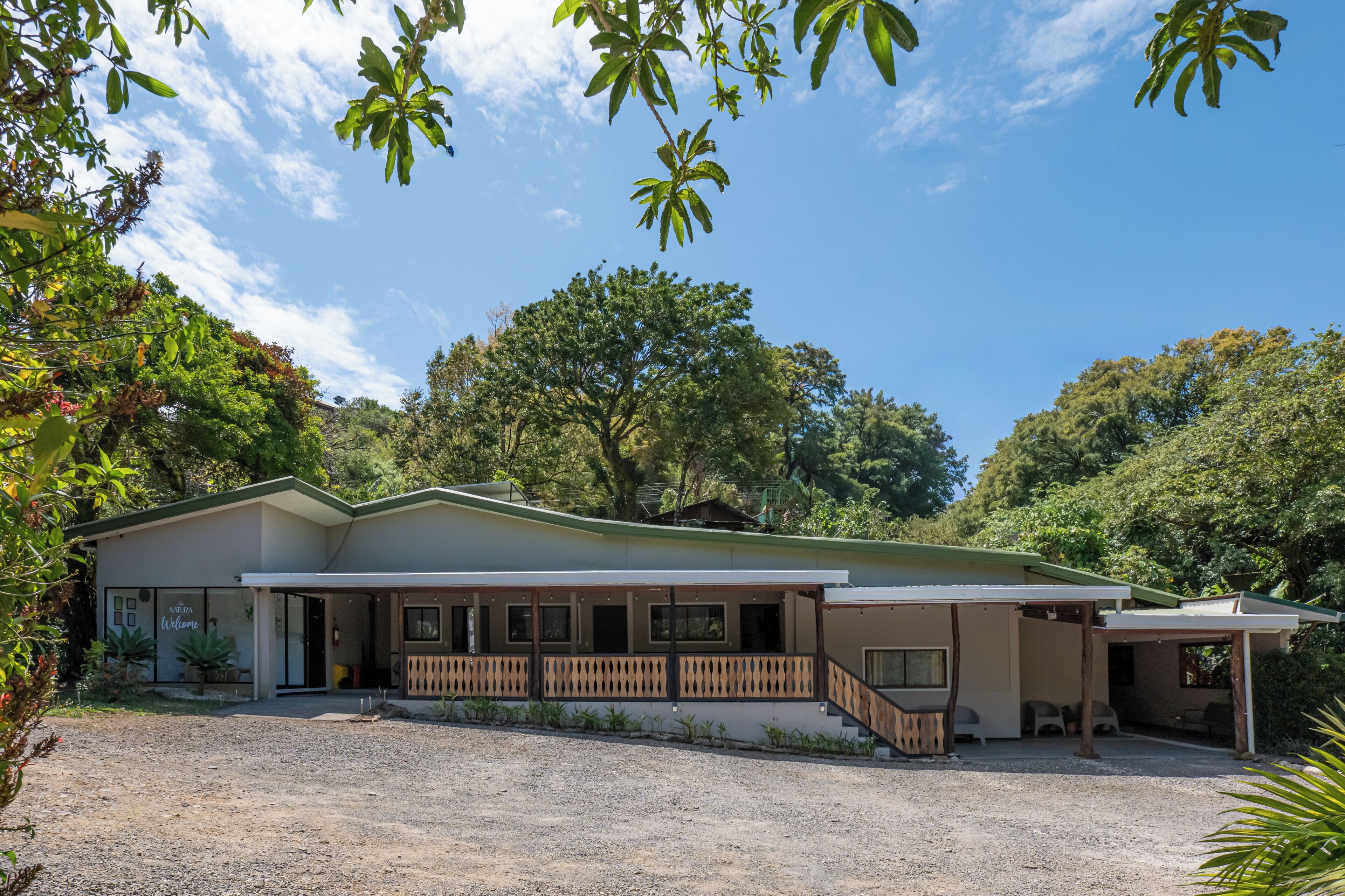 A two-story building with a covered porch, a gravel driveway, and surrounding trees.
