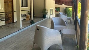 Un espacio al aire libre cubierto con mobiliario de mimbre, piso de madera y una estructura de pérgola.