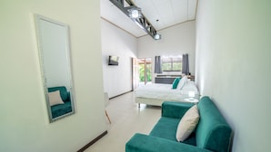 Una habitación de hotel con una cama grande, un sofá verde, un espejo y un televisor.