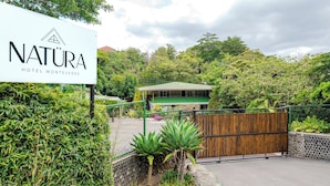 Letrero del Hotel Natura Monteverde, rodeado de exuberante vegetación y un portón de madera.