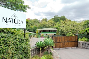 Une enseigne indiquant lâhĂŽtel Natura Hotel Monteverde, entourĂ©e dâune vĂ©gĂ©tation luxuriante et dâun portail en bois.