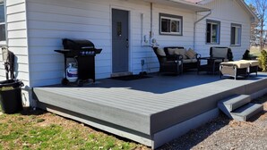 Una casa con veranda coperta, barbecue, mobili da giardino e un cestino.