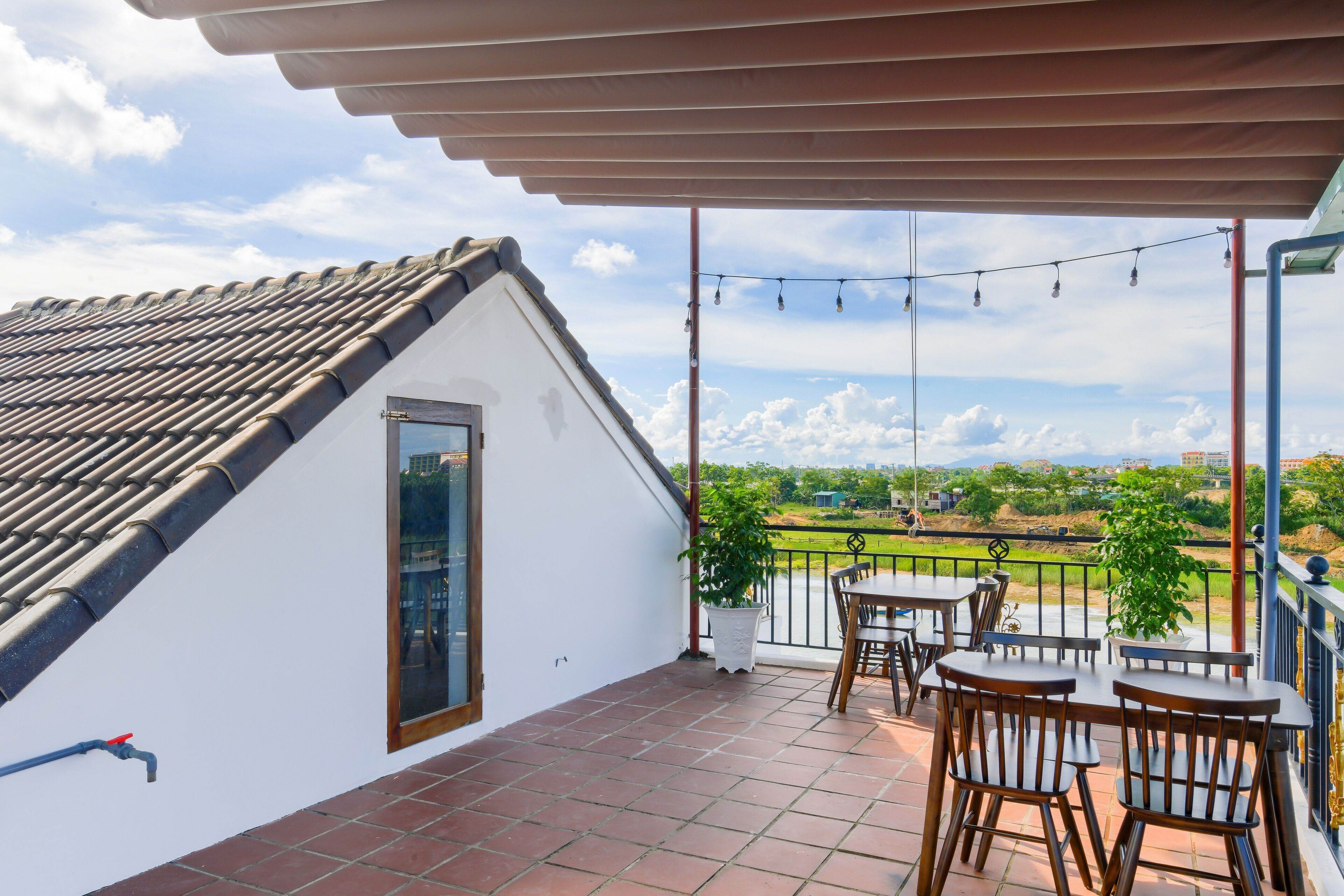 A terrace with a tiled floor, a table and chairs, a potted plant, and a view of the countryside.