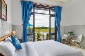 A hotel room with a bed, a small table with chairs, and a balcony with a view of greenery and a body of water. - Gio Chieu Homestay (Da Nang)