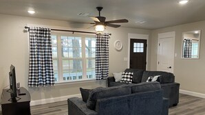 A living room with a dark gray sofa, a flat-screen TV, and a ceiling fan.