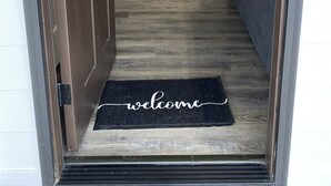 A wooden door with a black doormat that reads "welcome".