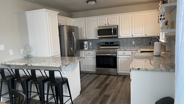 A modern kitchen with white cabinetry, stainless steel appliances, a granite countertop, and a bar area with stools.