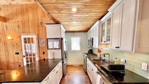 A modern kitchen with wooden paneling, white cabinets, and a black countertop. - Your Vermont Mountain Haven Pet Friendly home with Hot tub! (Winhall)